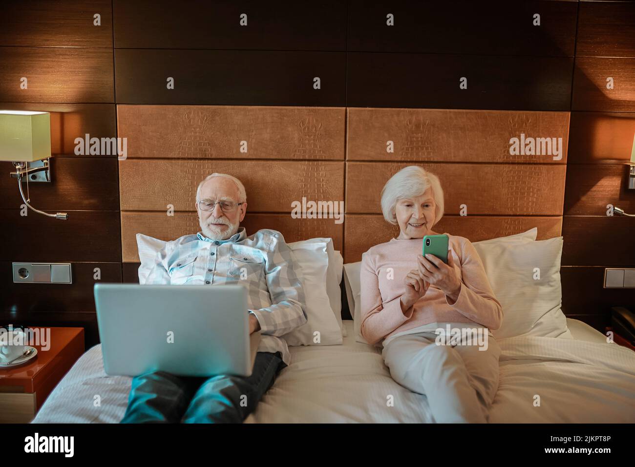 Senior couple lying in bed with their gadgets in hands Stock Photo