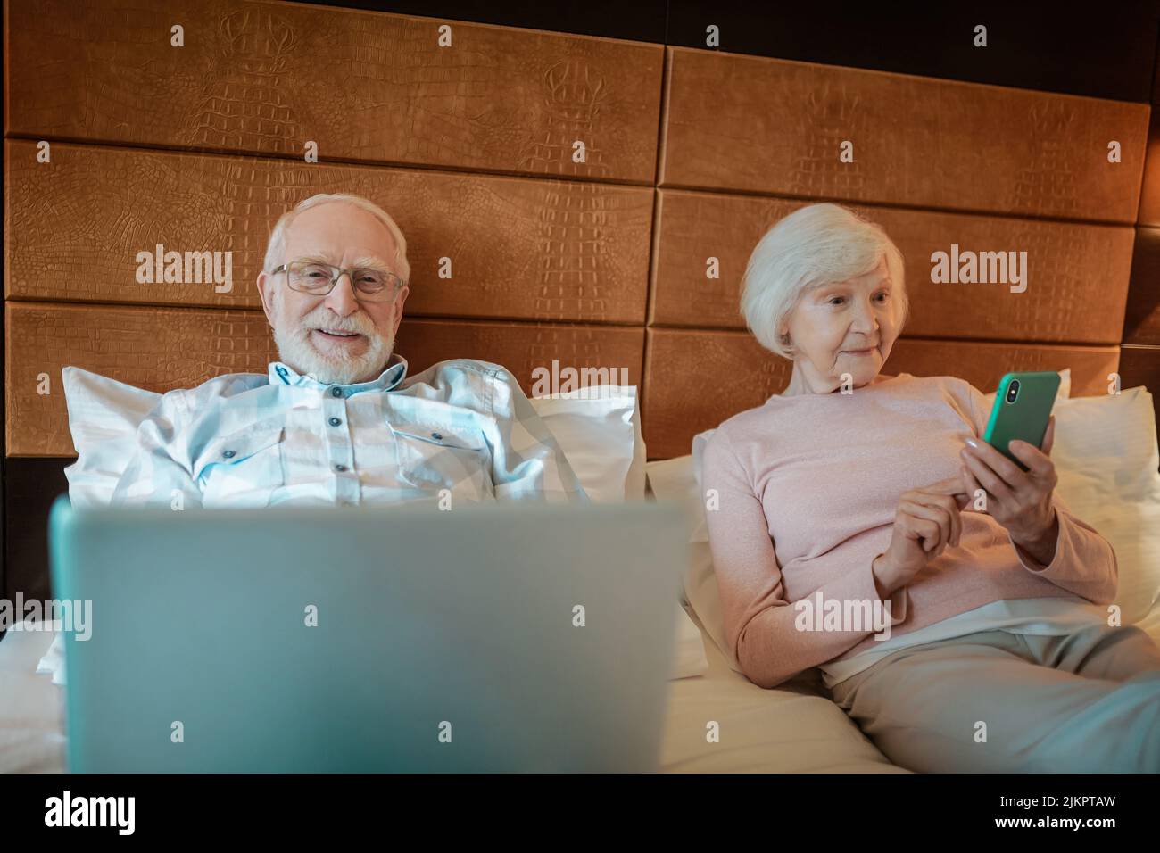 Senior couple lying in bed with their gadgets in hands Stock Photo