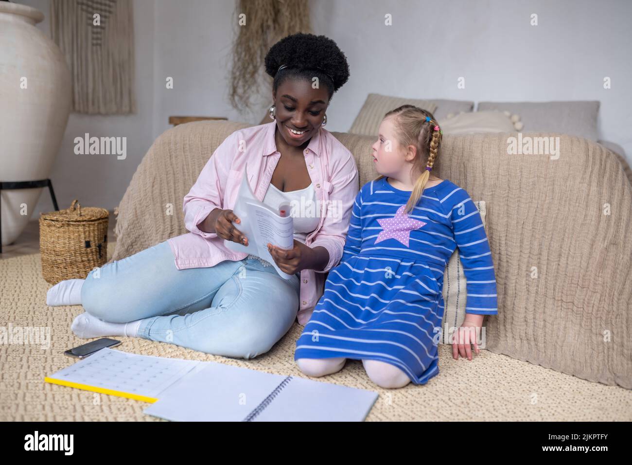 Dark-skinned woman reading something to a girl with down syndrome Stock Photo