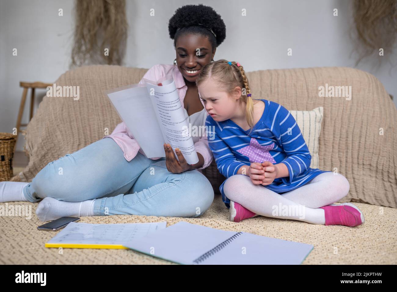 Dark-skinned woman reading something to a girl with down syndrome Stock Photo