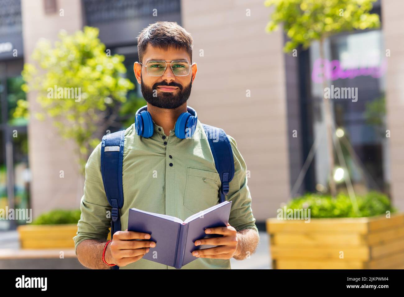 indian student with blue headset and backpack holding books at sunny day Stock Photo