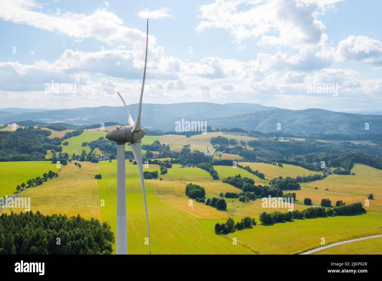 Aerial view of wind turbines propeller in the yellow field with amazing view on the mountains in sunny day. Environment friendly and renewable energy resource.  Stock Photo