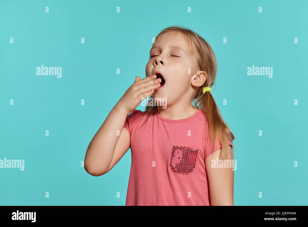 Close-up shot of beautiful blonde little girl in a pink dress posing against a blue background. Stock Photo