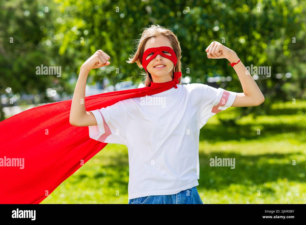 Funny teenager girl playing power super hero over green park background Stock Photo