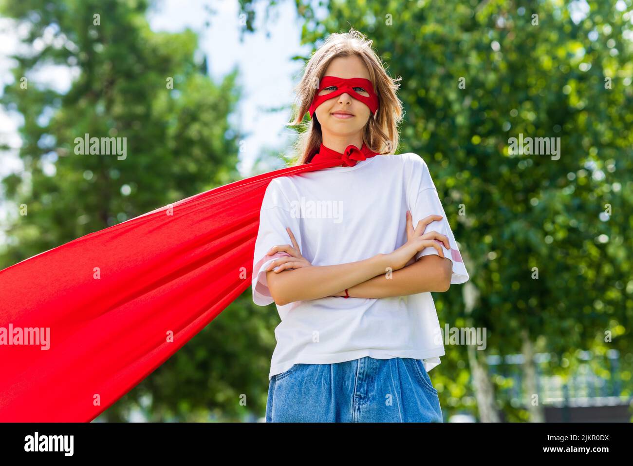 Funny teenager girl playing power super hero over green park background Stock Photo