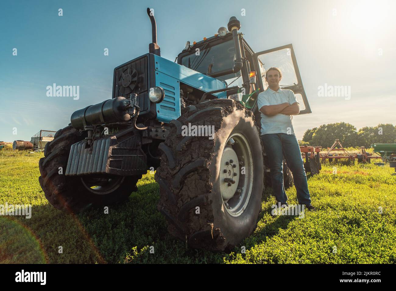 Farmer stands by tractor in agricultural fields and land. Farming, growing vegetables and fruits, harvesting. Stock Photo