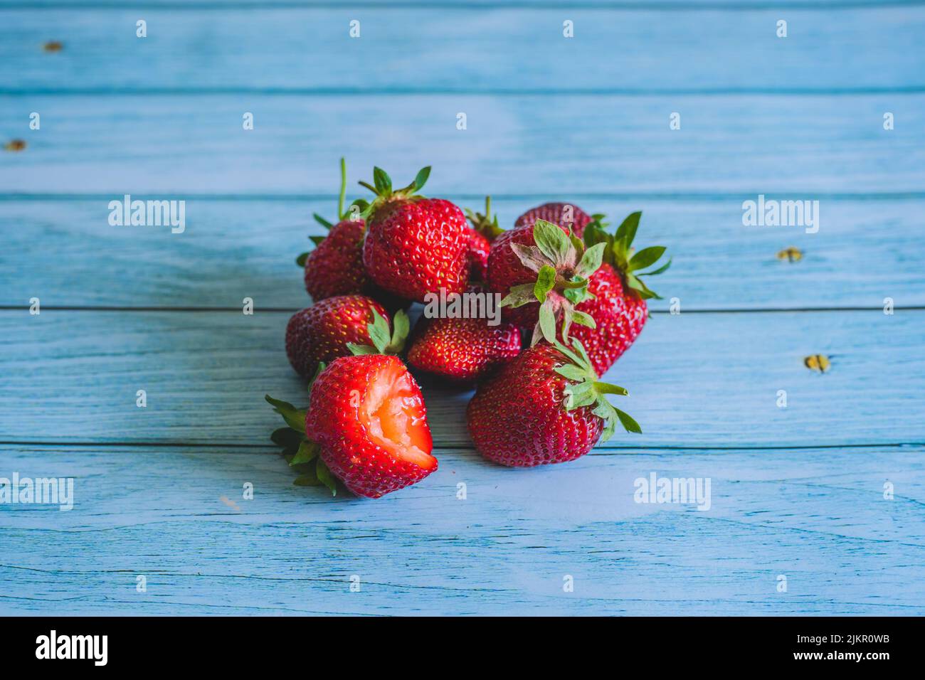 Fresh bitten strawberry. Ripe sweet strawberries on blue wooden table. Summer fruits concept.Food and drink space for text. Close up of red berries. H Stock Photo
