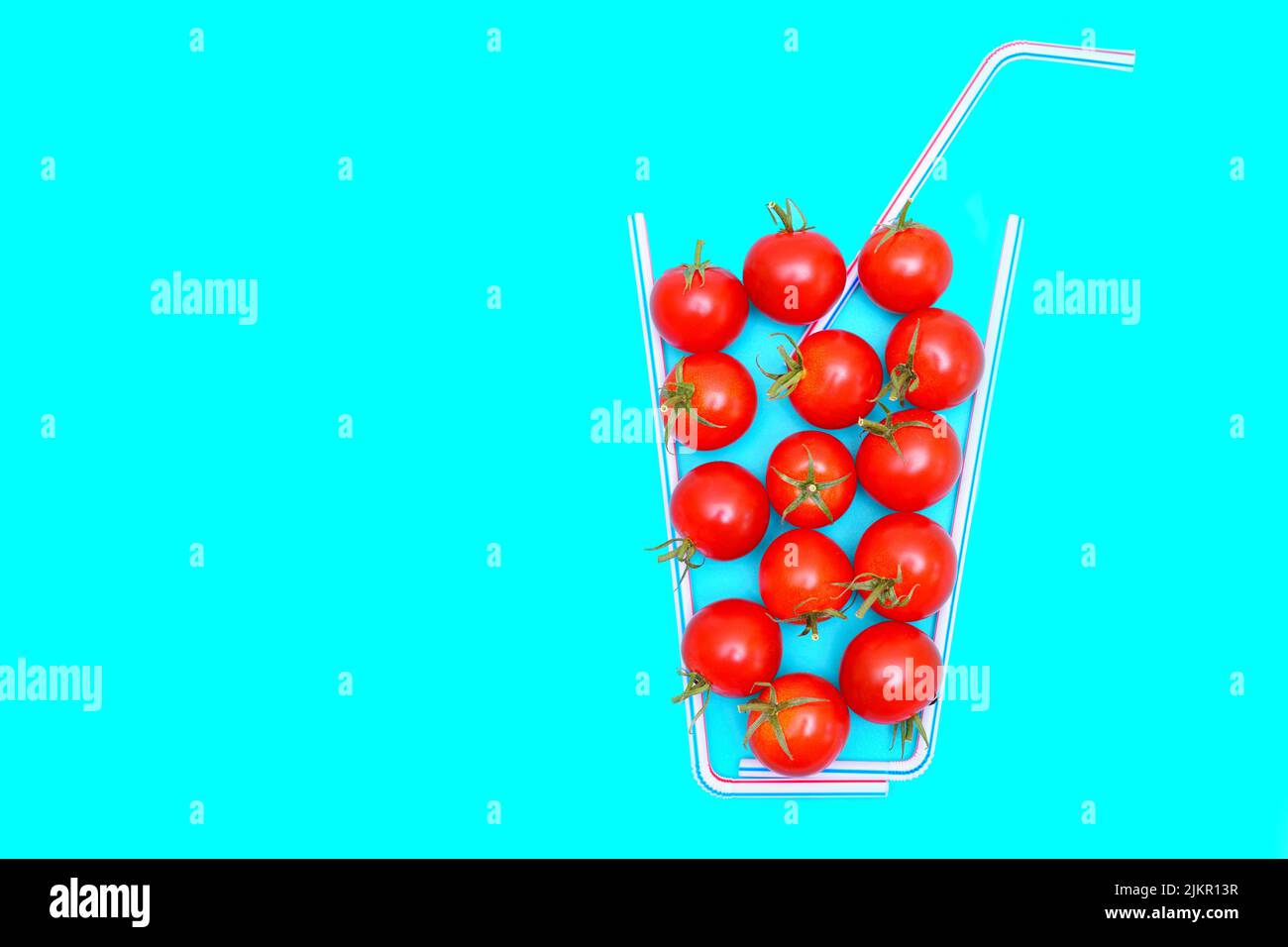 Cocktail tomatoes and drinking straws arranged into a juicy composition on blue background with copy space. Stock Photo
