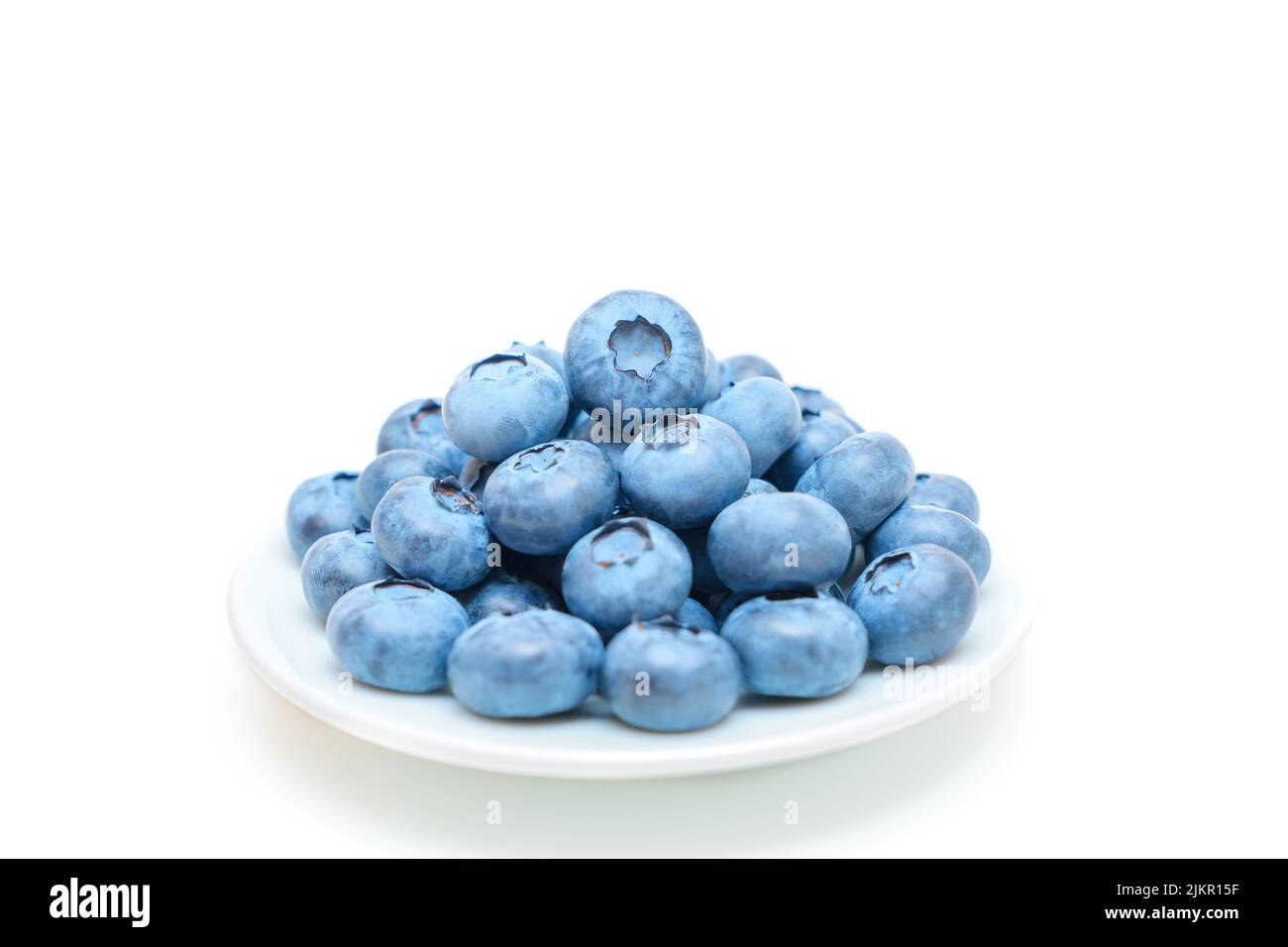 Pile of fresh ripe blueberries on a white saucer isolated on white background, selective focus. Stock Photo