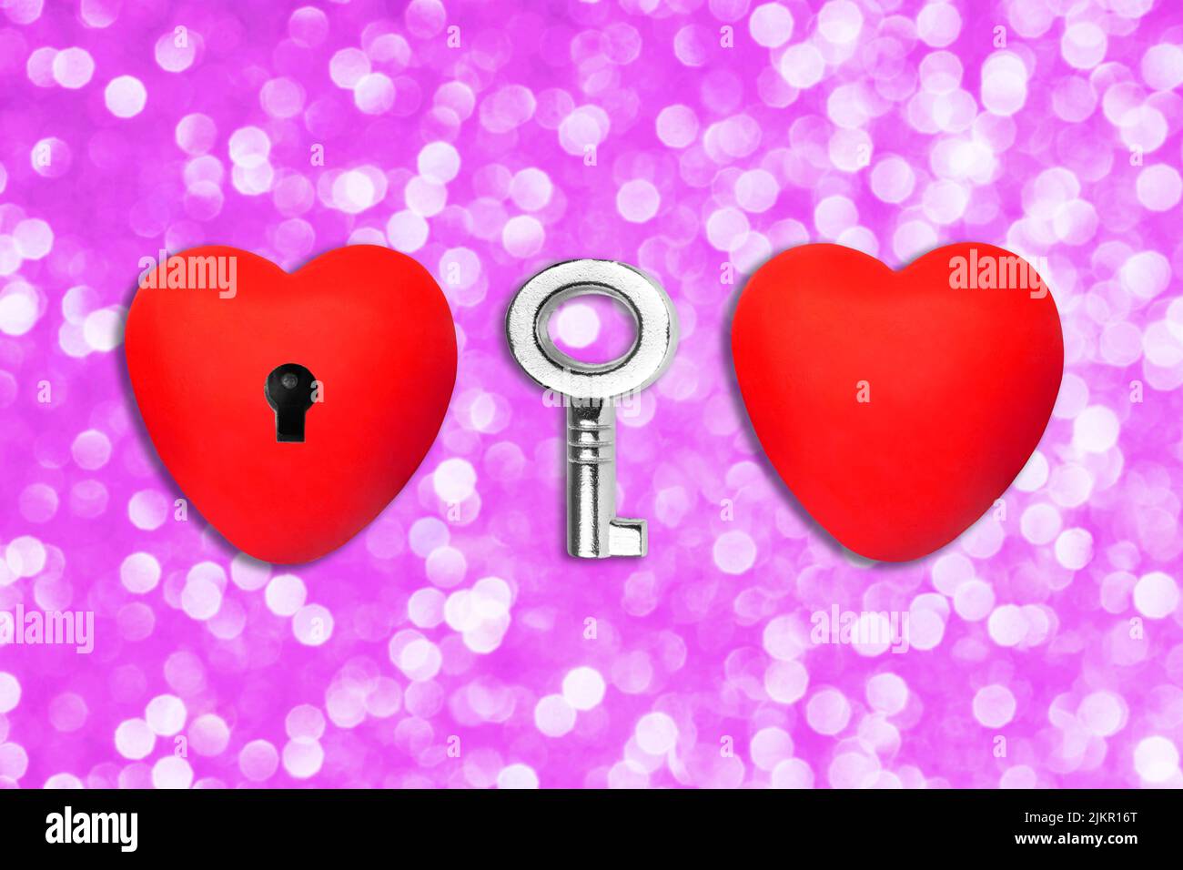 Two red heart shapes and a skeleton key on dreamy pink background with bokeh effect. One heart has a keyhole. Stock Photo