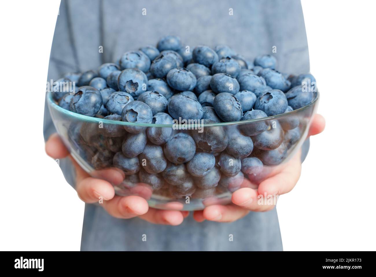 Woman wearing a matching dress holds a large glass bowl of fresh ripe blueberries isolated on white background, wide angle, selective focus. Stock Photo