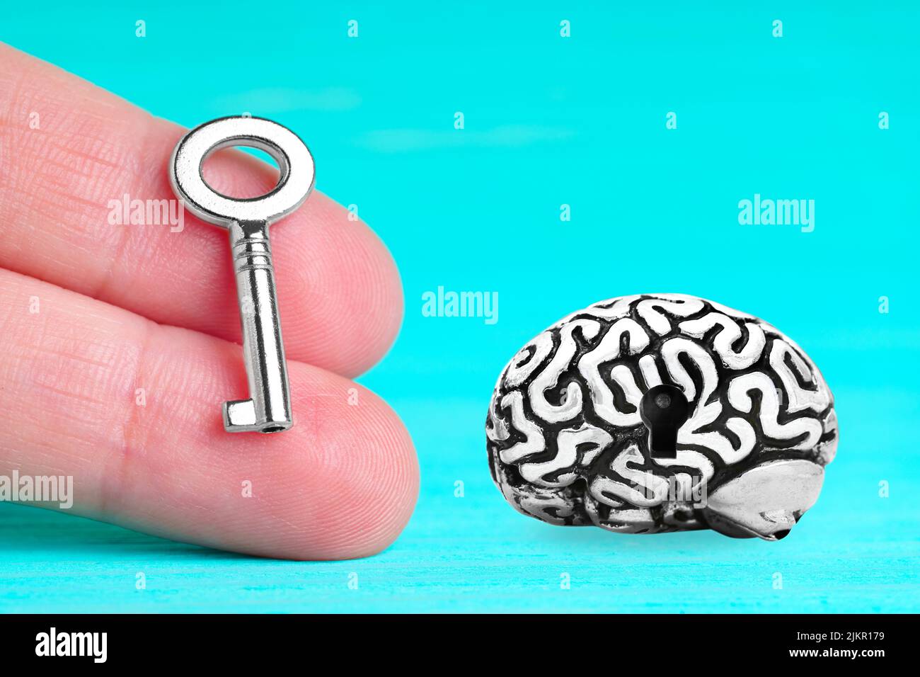 Anatomical copy of a human brain having a keyhole and a small master key in hand isolated on blue background. Unlock secrete power of the brain. Stock Photo