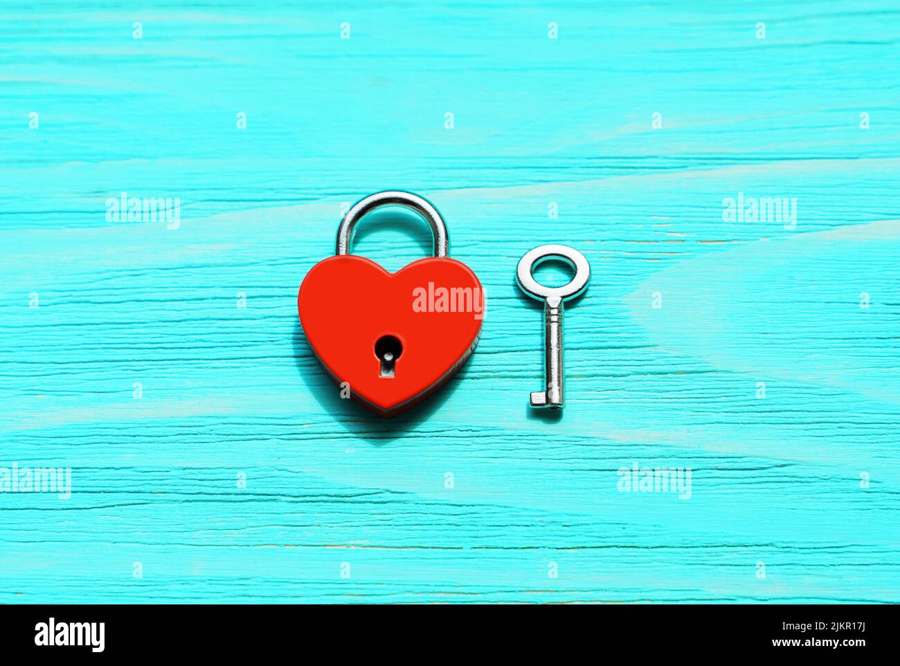 Red heart-shaped padlock and silver-toned skeleton key on a blue wooden background with copy space. Strong romantic relationships concept. Stock Photo