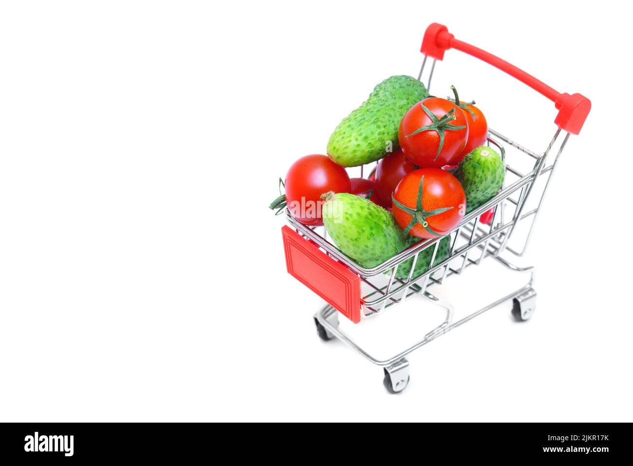Pile of fresh cucumbers and cherry tomatoes in a miniature shopping trolley isolated on white background. Veggies straight from the farm. Stock Photo