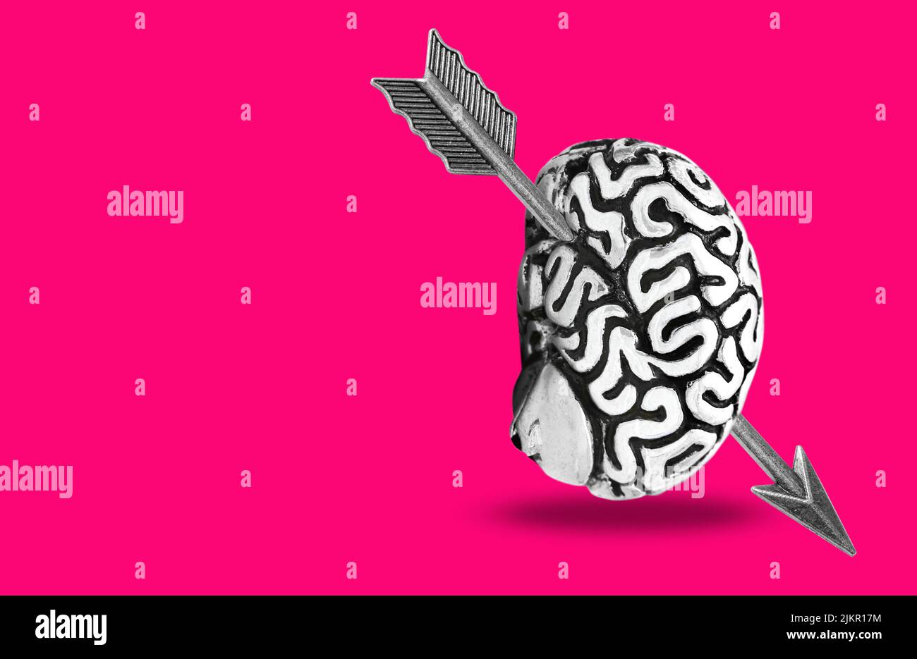 Steel feathered arrow gone through a human brain isolated on pink background. First sight affection concept. Stock Photo