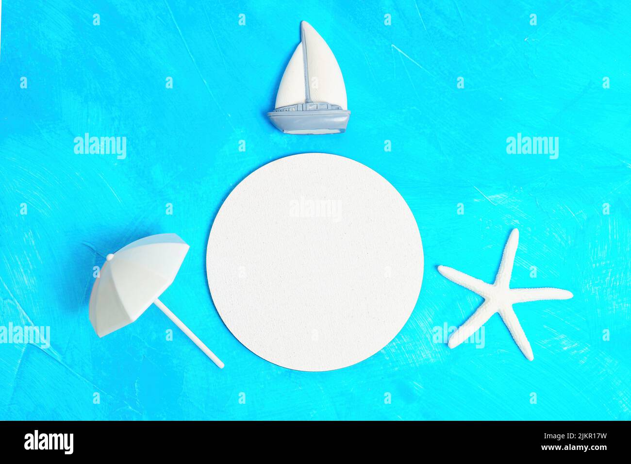 Creative summer vacation background with copy space made from a sea star, ship and sun umbrella props placed on blue background imitating water. Stock Photo