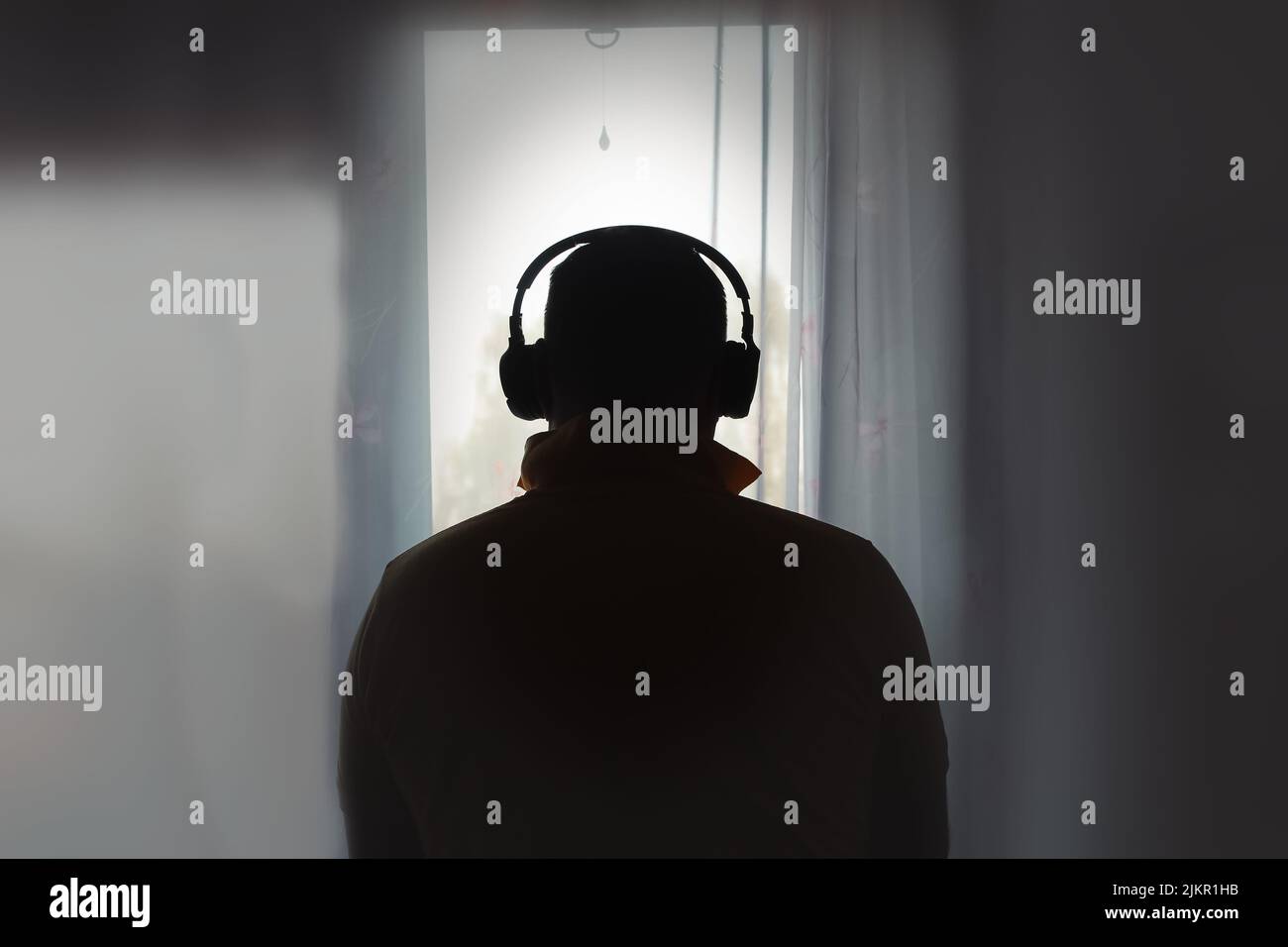Man In Headphones Looks Out Window. Back View. Stock Photo