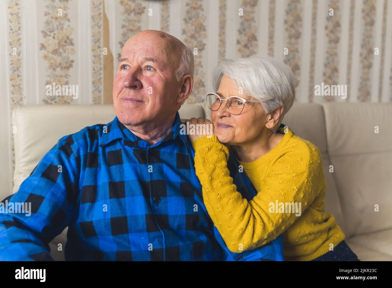 Portrait of an elderly couple - caring husband standing behind his happy loving wife and hugging her, and a woman herself softly touching his arm. High-quality photo Stock Photo