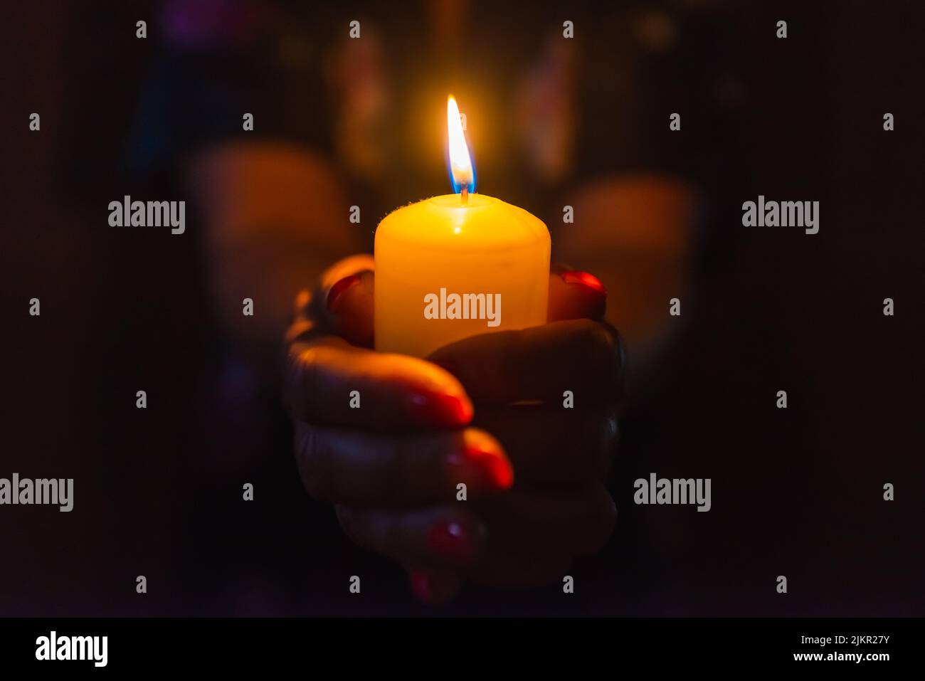 Candle in female hands on black dark background.Prayers candle in hands. Stock Photo