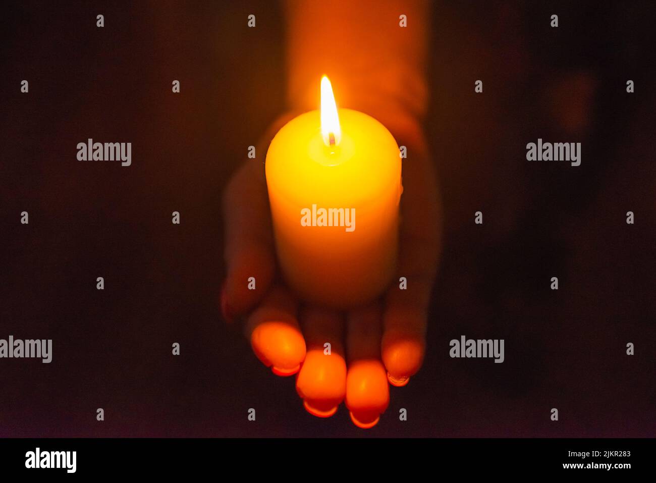 Candle in female hands on black dark background.Prayers candle in hands