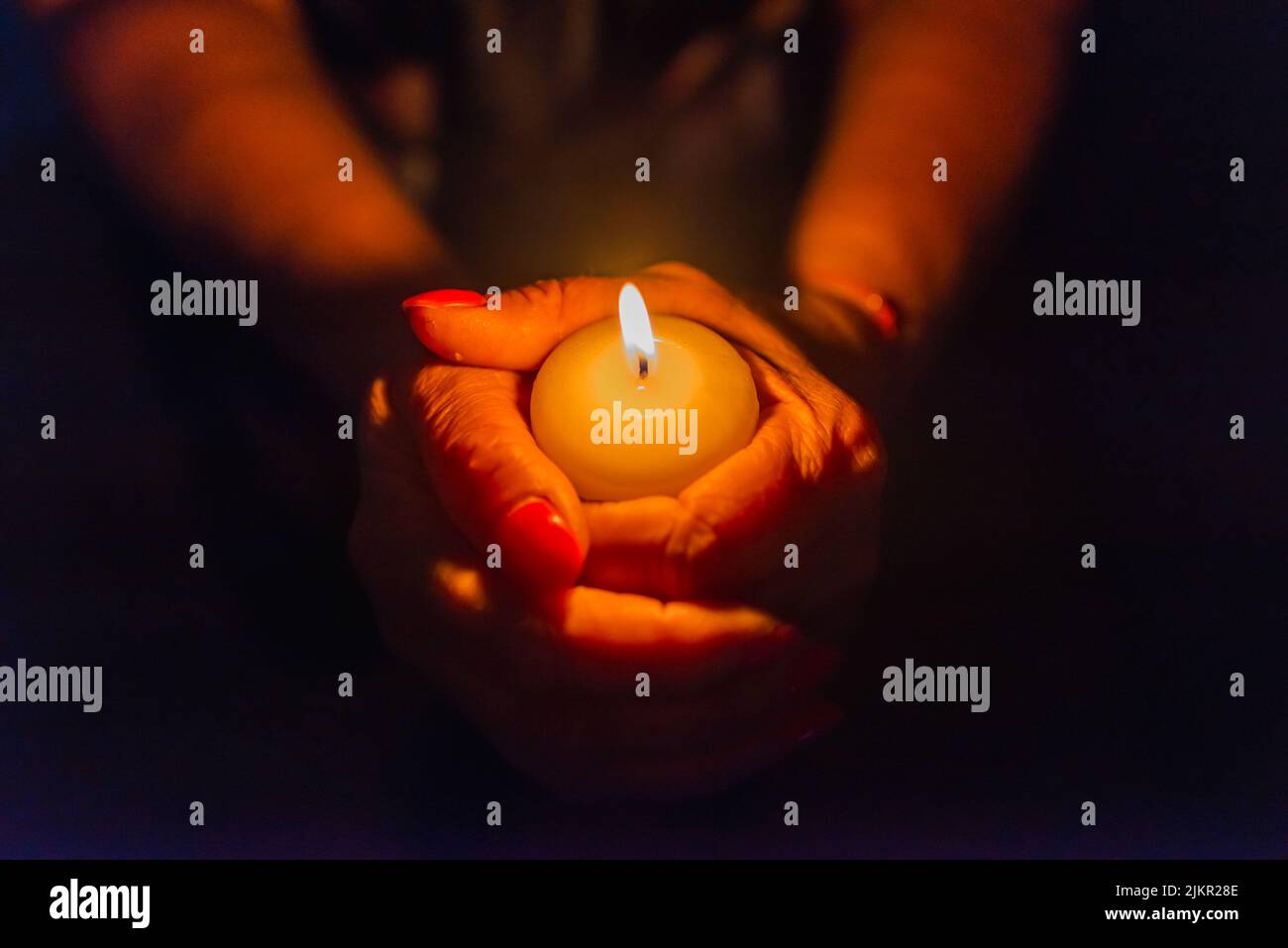 Candle in female hands on black dark background.Prayers candle in hands
