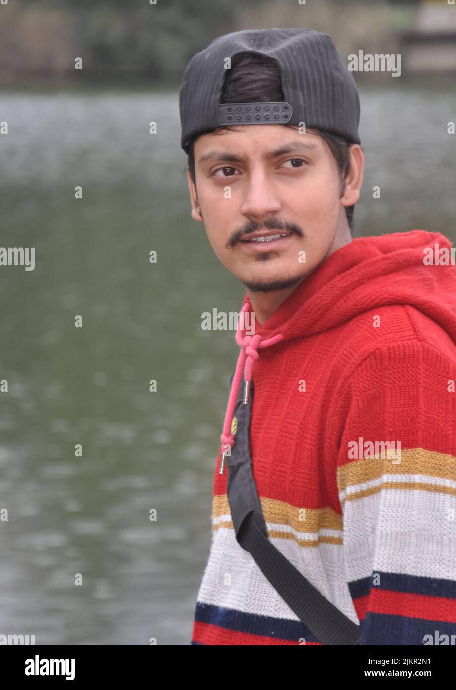 Waist-up of a Indian young guy wearing cap backwards looking sideways while standing by the lake Stock Photo