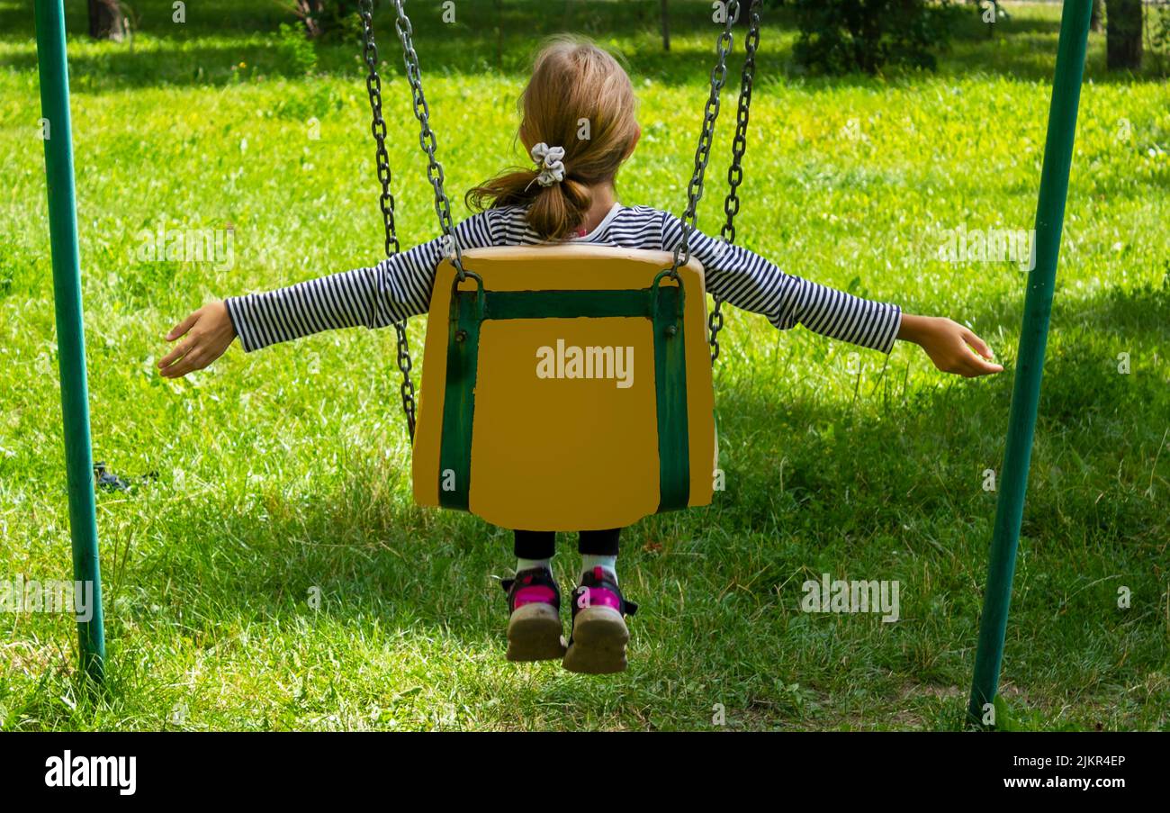 Little girl sits with her back on a swing and rides in summer Stock Photo