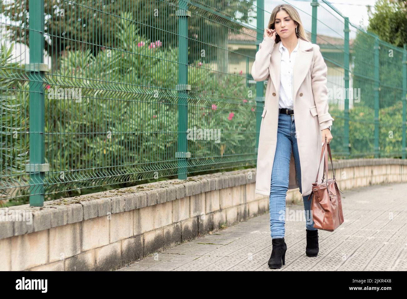 business woman walking down the street with a brown bag a beige coat ...
