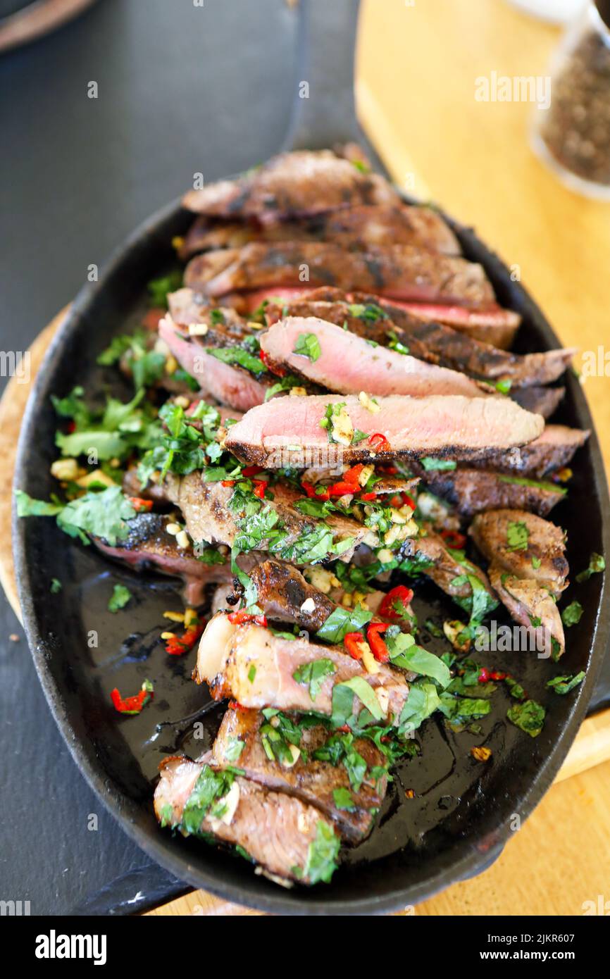Sliced Ribeye Steak with coriander, garlic and chillies in a hot skillet Stock Photo