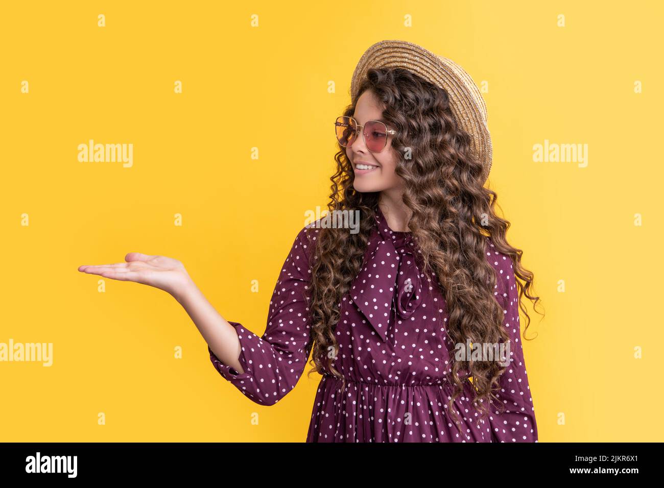 smiling girl in straw hat and sunglasses with long brunette curly hair on yellow background Stock Photo