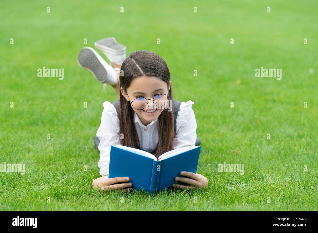 Reading time. Happy teen girl reading book lying on grass after school, reading. Stock Photo