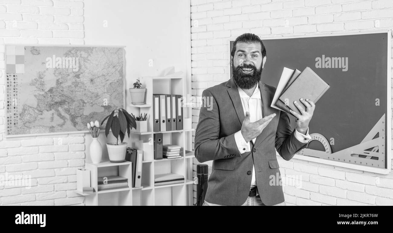 reason for training. back to school. informal education. happy mature teacher showing books from library. bearded man work in classroom with workbook Stock Photo
