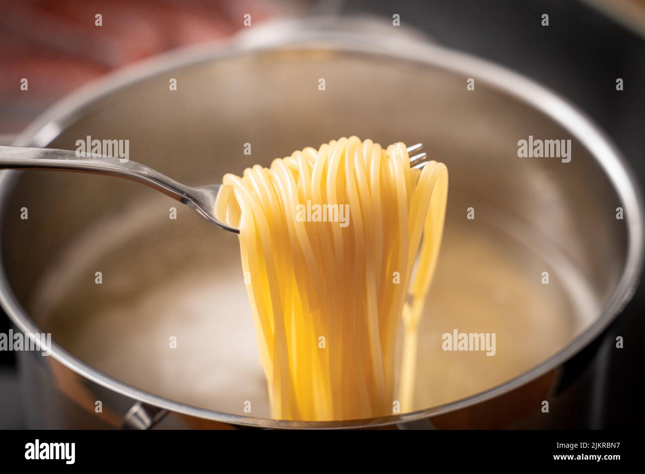 Spaghetti Noodles Are Boiling In A Pot Of Water On A Stove In The Kitchen. Pasta On A Fork To Test The Pasta For All Dente Stock Photo