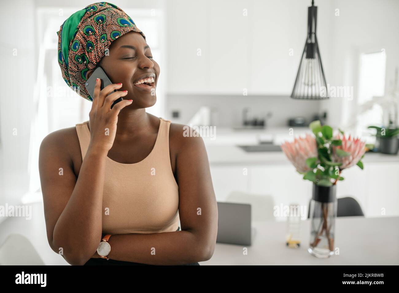 Beautiful African woman at home, smiling and laughing, using mobile smart phone, wearing traditional headscarf and looking into distance with copy spa Stock Photo