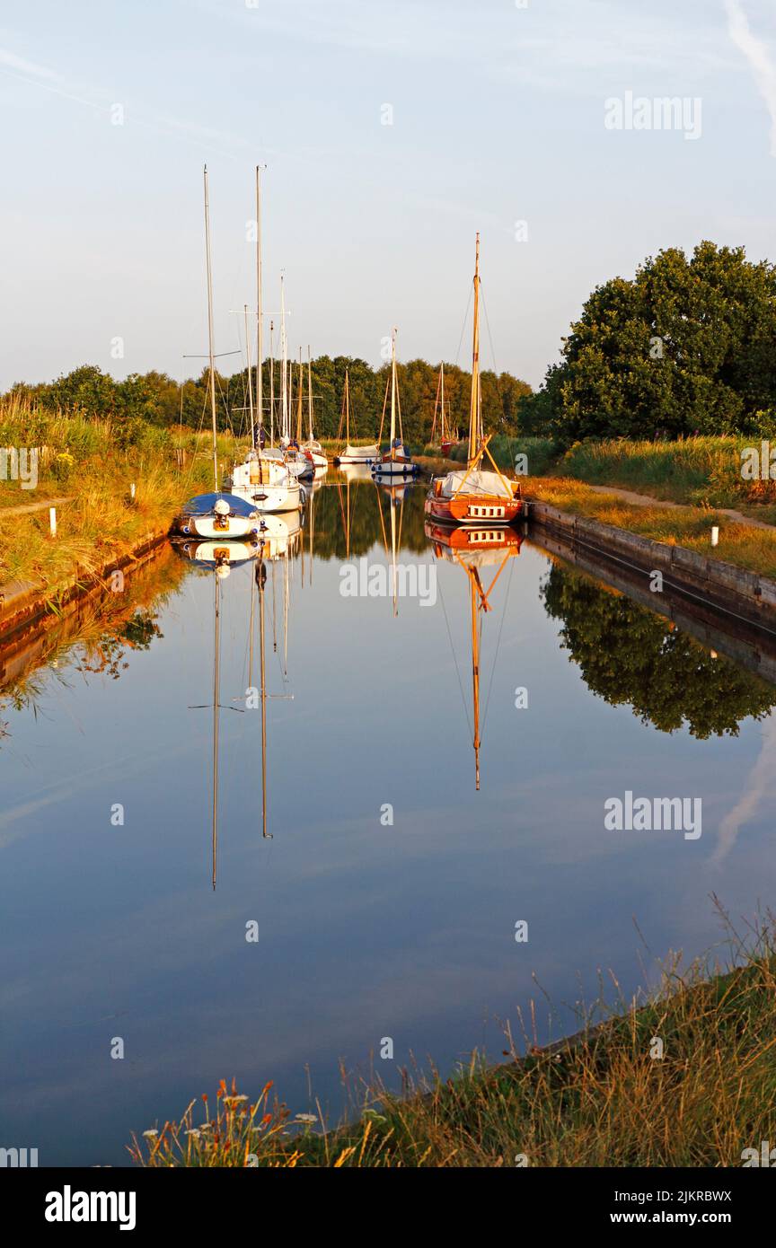 A view of boats moored in Horsey Dyke with reflections and access to Horsey Mere on the Norfolk Broads at Horsey, Norfolk, England, United Kingdom. Stock Photo