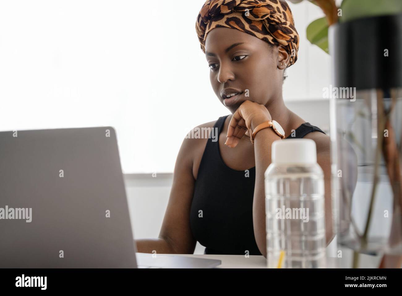 Beautiful young African woman wearing tradition headscarf. Sitting at home working on laptop. Stock Photo