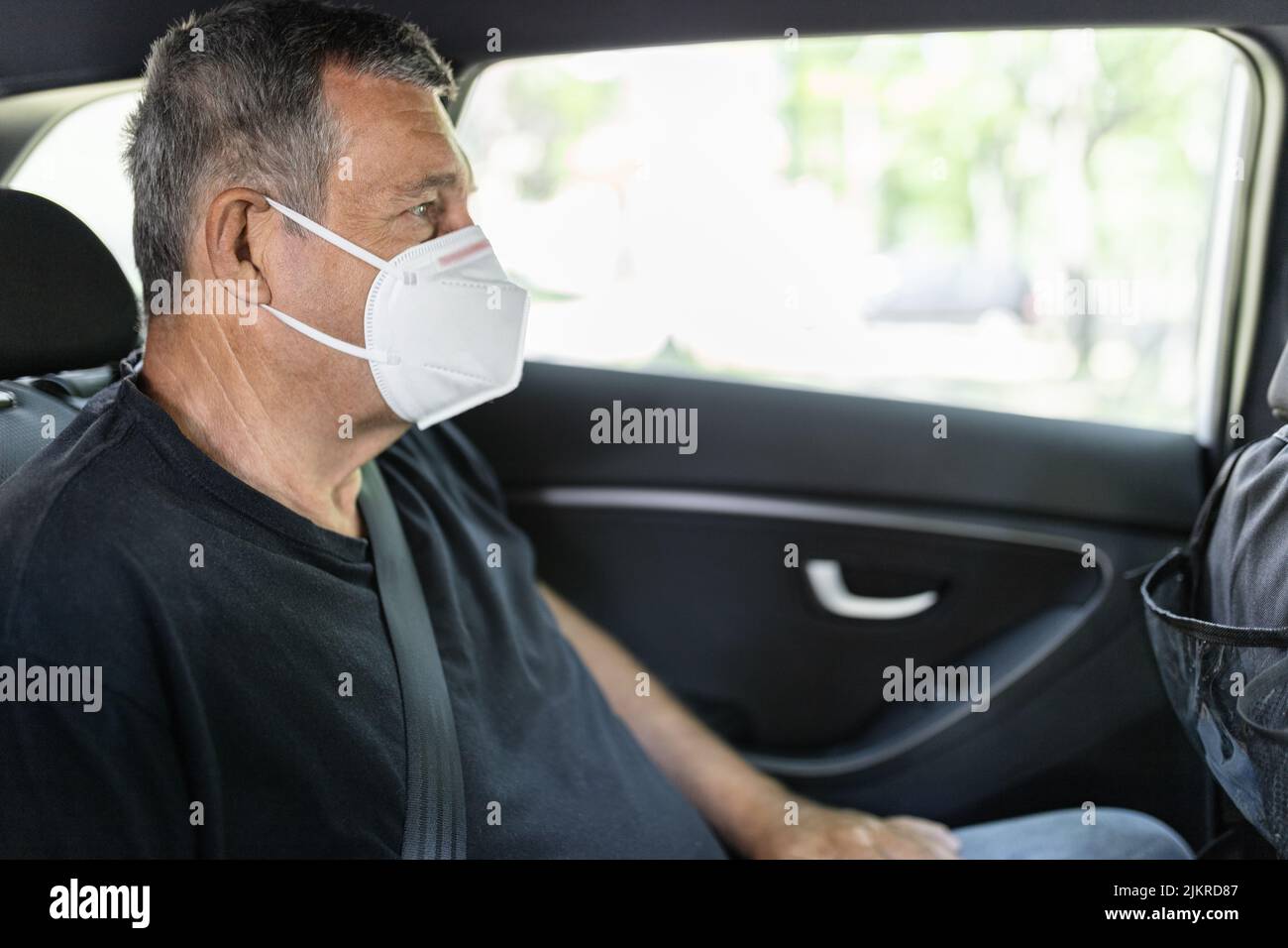 Senior in his 70s sitting at the back of car wearing a face mask for protection against corona virus Stock Photo