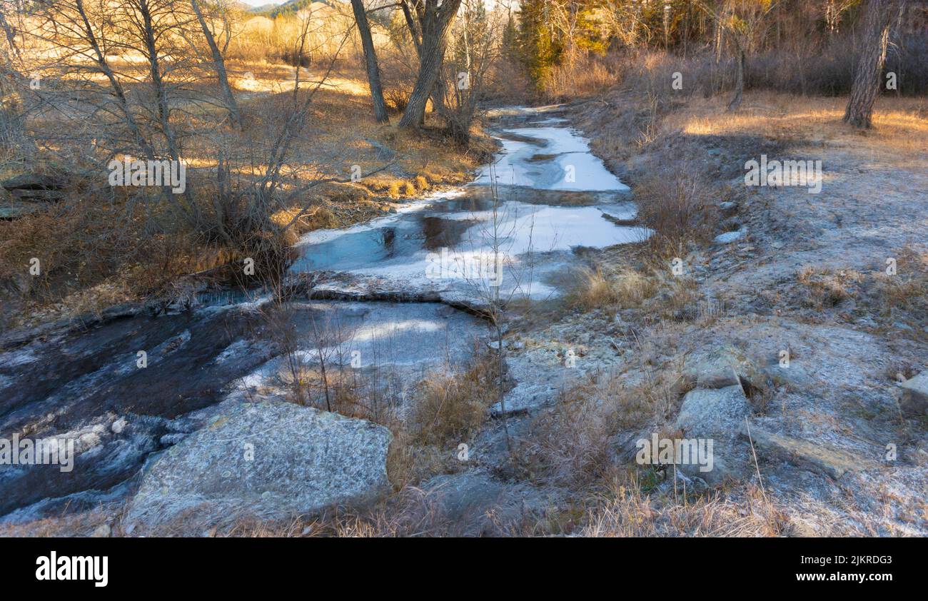 Dusting of snow on the ground next to a Montana stream with ice Stock