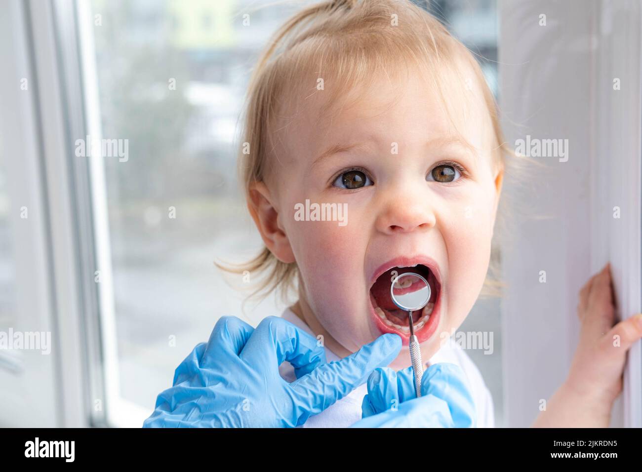 Closeup open mouth child and mirror in dentists hands in blue gloves