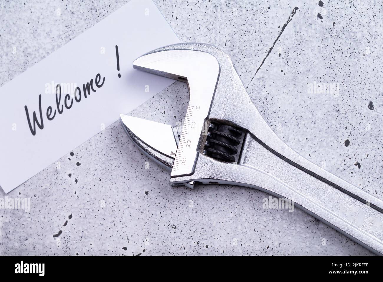 The photo shows a label with the words 'welcome' with a wrench on a grey background Stock Photo