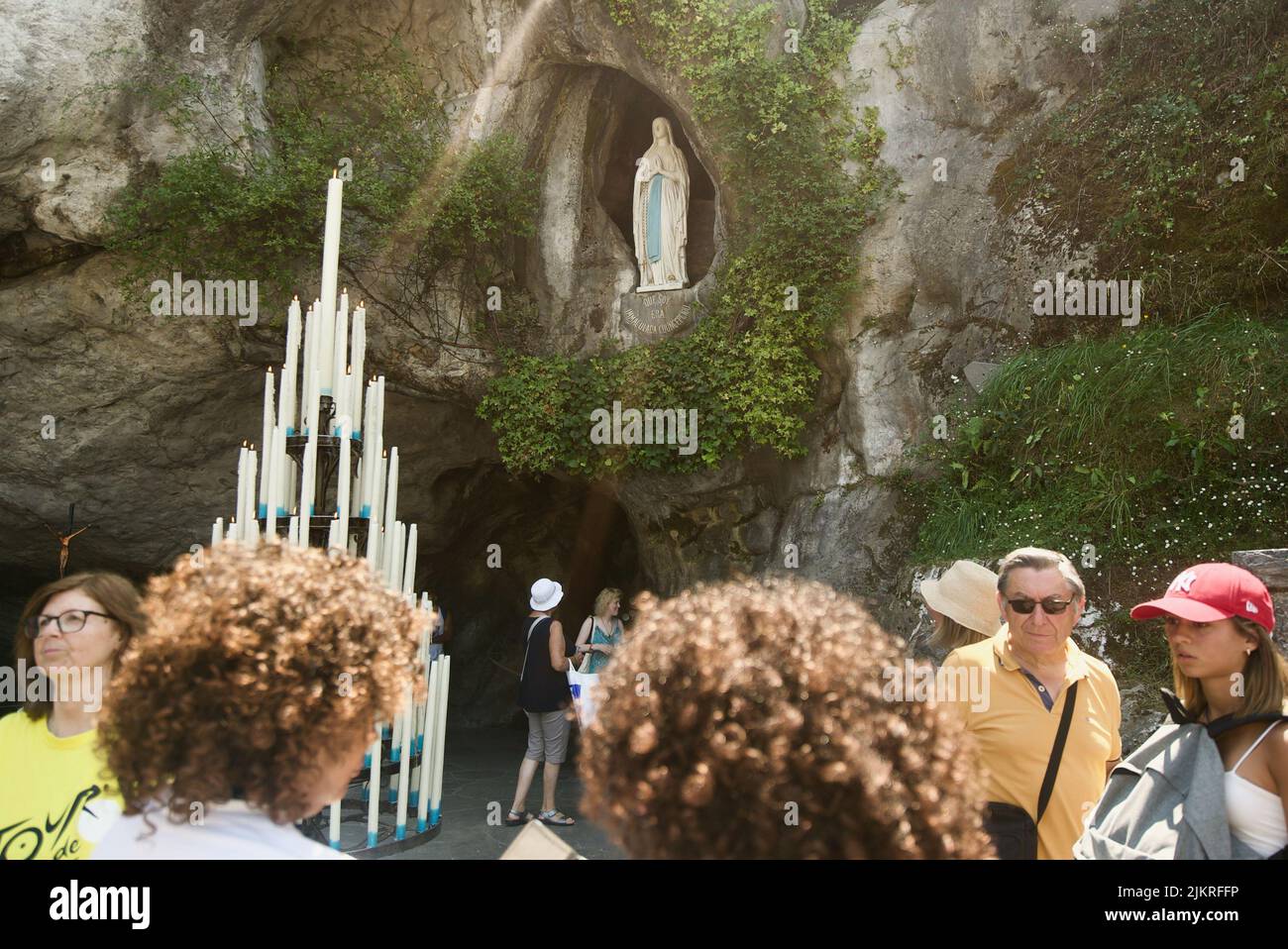 People gathered at the Grotto of Massabielle/Grotto of the Apparitions at Sanctuary of Our Lady of Lourdes, Pilgrimage. (Virgin Mary statue in Grotto) Stock Photo