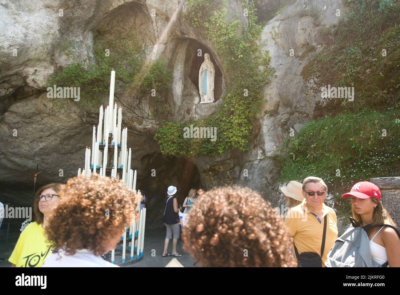 People gathered at the Grotto of Massabielle/Grotto of the Apparitions at Sanctuary of Our Lady of Lourdes, Pilgrimage. (Virgin Mary statue in Grotto) Stock Photo