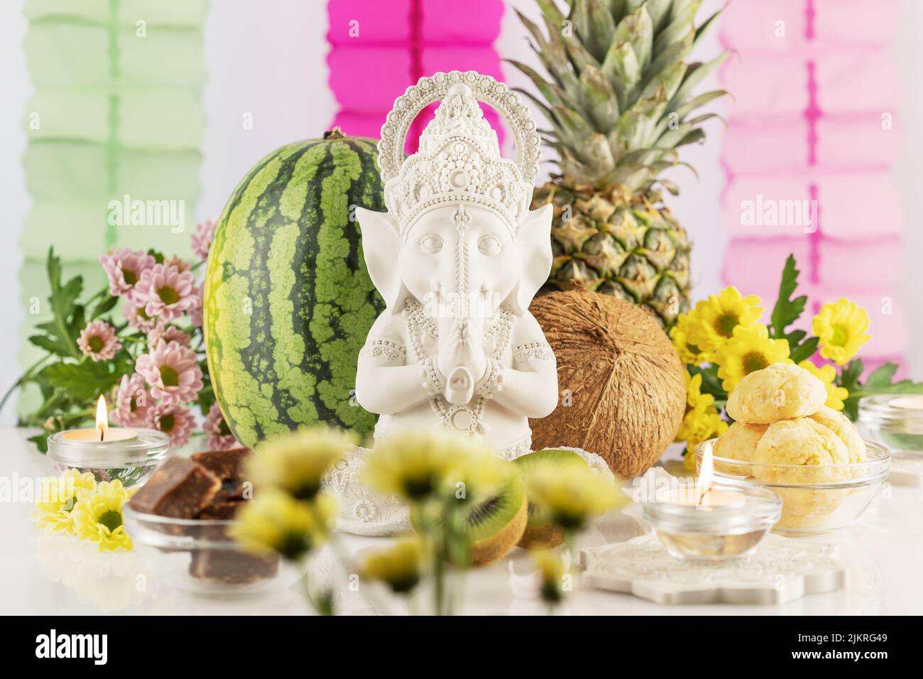 Sculpture of Lord Ganesha with offerings, fruits, sweets, flowers and candles on a light