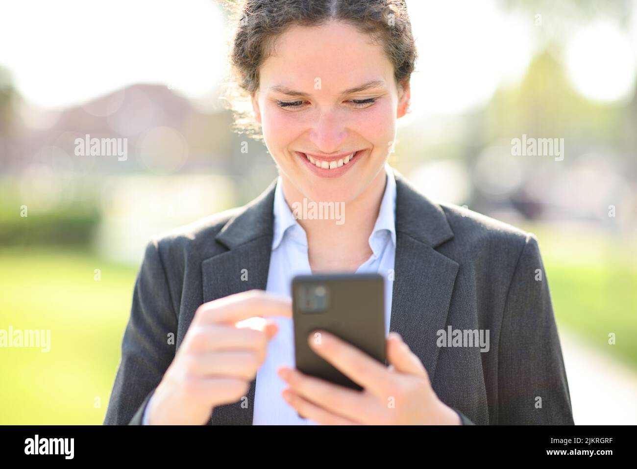 Front view portrait of a happy businesswoman walking checking smart phone outside Stock Photo