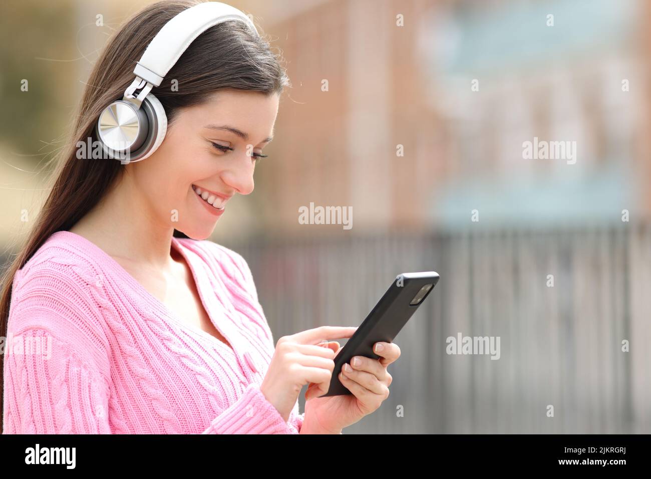 Happy teen wearing headphones listening to music using phone in the street Stock Photo