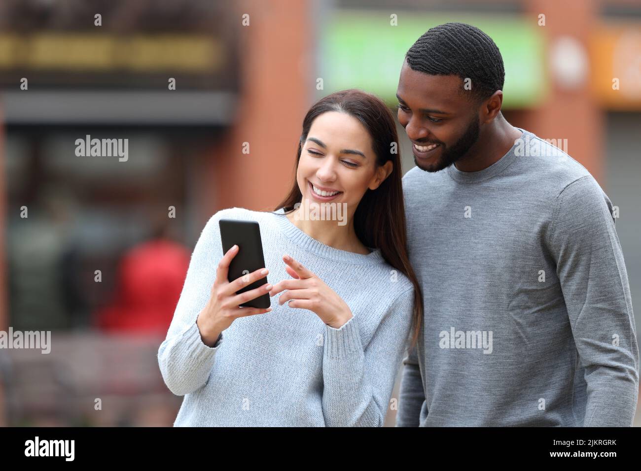 Happy interracial couple checking cell phone in the street Stock Photo