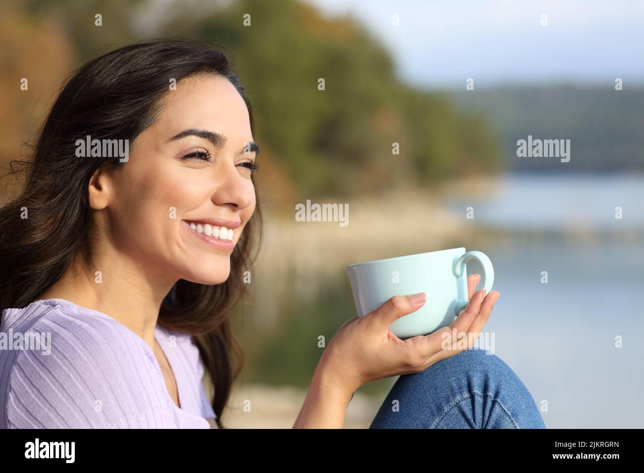 Smiling woman with coffee cup sitting on jetty stock photo