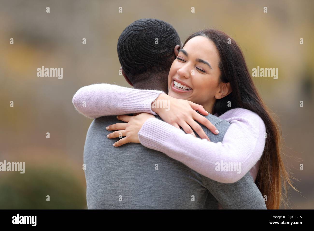 Happy woman meeting and hugging a man with black skin in a park Stock Photo