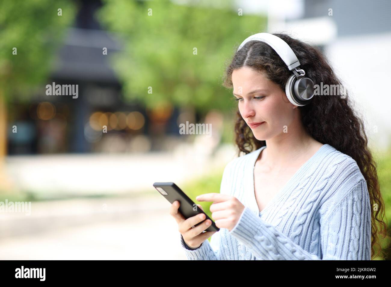 Woman walking using smart phone and wearing headphones to listen to music in the street Stock Photo