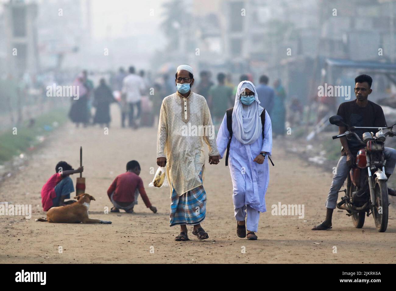 People walk along a road beside a smoky industrial area in Dhaka, Bangladesh, August 3, 2022. REUTERS/Mohammad Ponir Hossain Stock Photo